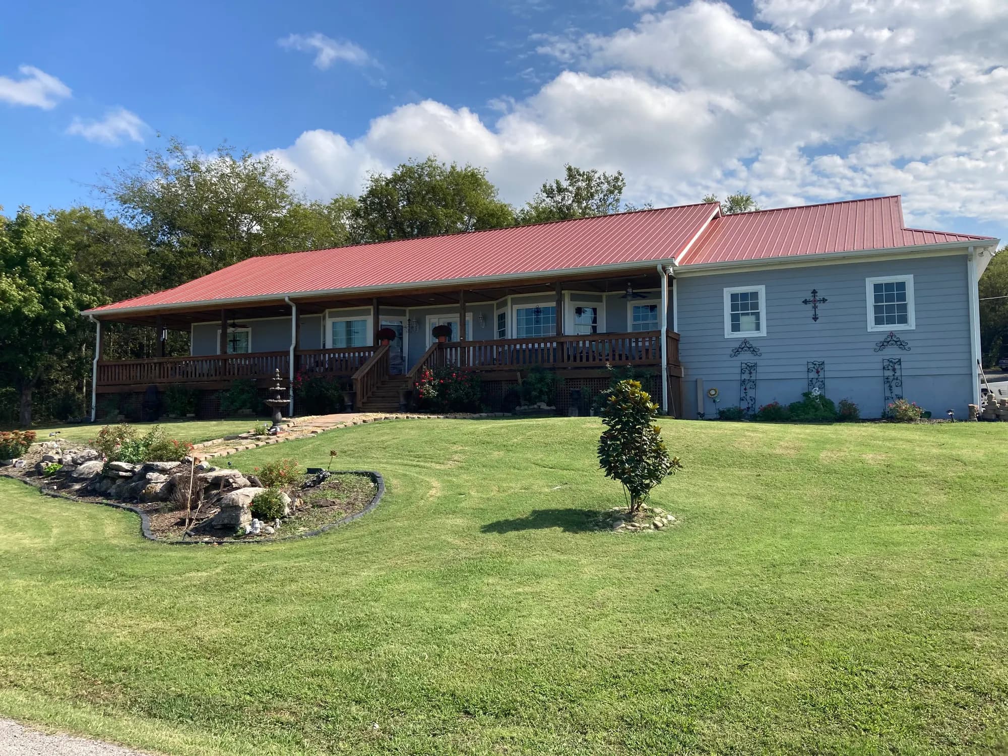 Single-story home with a red metal roof and a wraparound wooden porch after a completed roofing installation