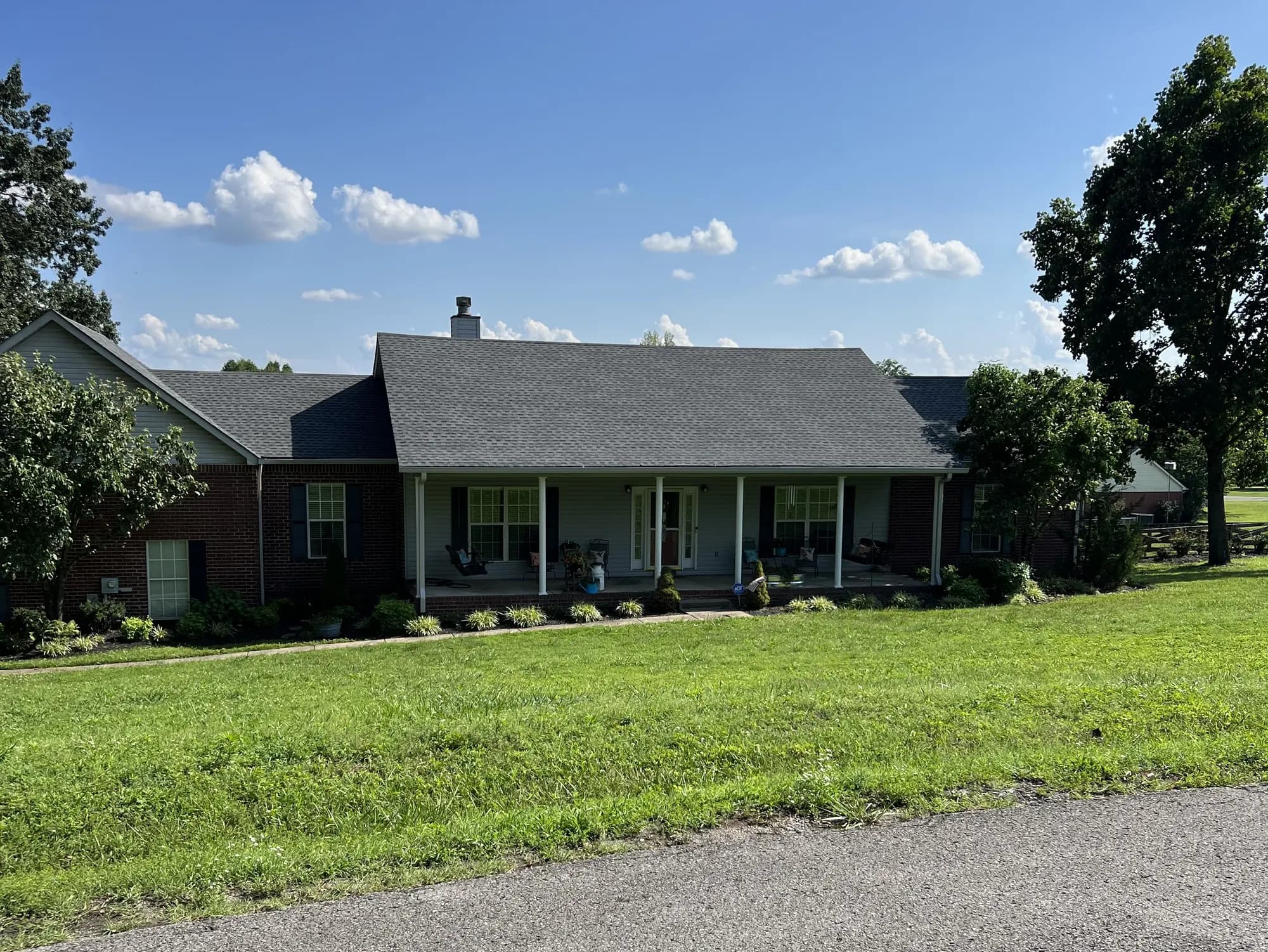 A single-story brick ranch-style home with a newly installed gray asphalt shingle roof and covered front porch