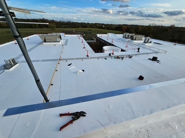 Wide view of a newly installed white TPO membrane roof with rooftop units and hills on the horizon at dusk