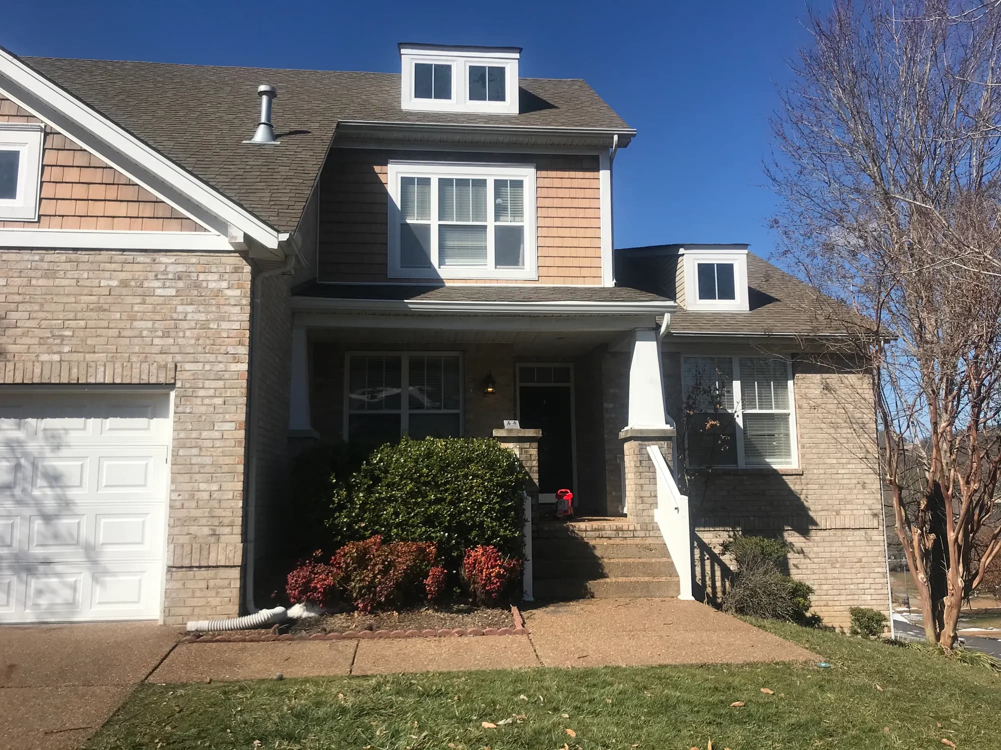 A two-story brick and shingle-style home with a covered front porch, dormer windows, and landscaped entrance