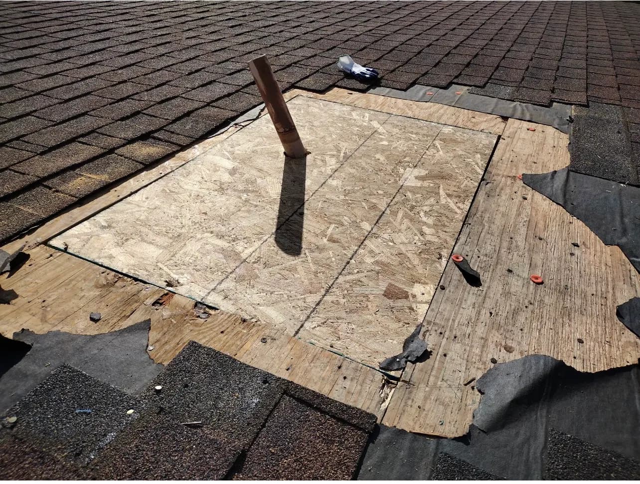 Roof repair in progress showing exposed plywood decking around a vent pipe, with shingles and underlayment around it