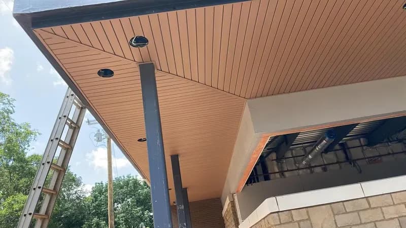 Newly installed tan soffit and fascia on a commercial building, with a ladder and stone facade below