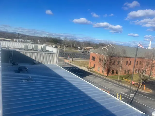 New light gray metal roof on a commercial building overlooking a brick office building and a street