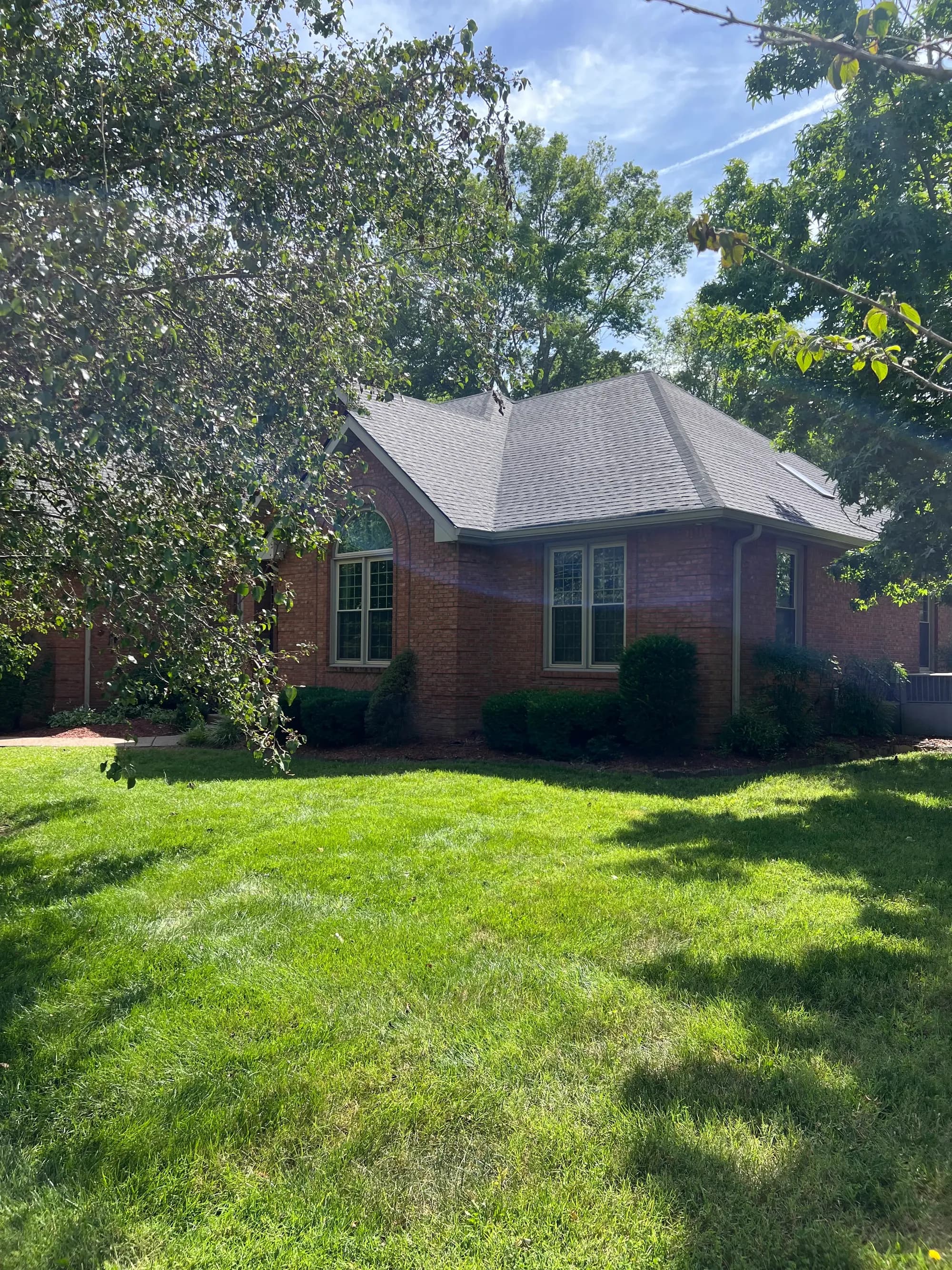 A brick house with a newly installed gray shingle roof, framed by mature trees