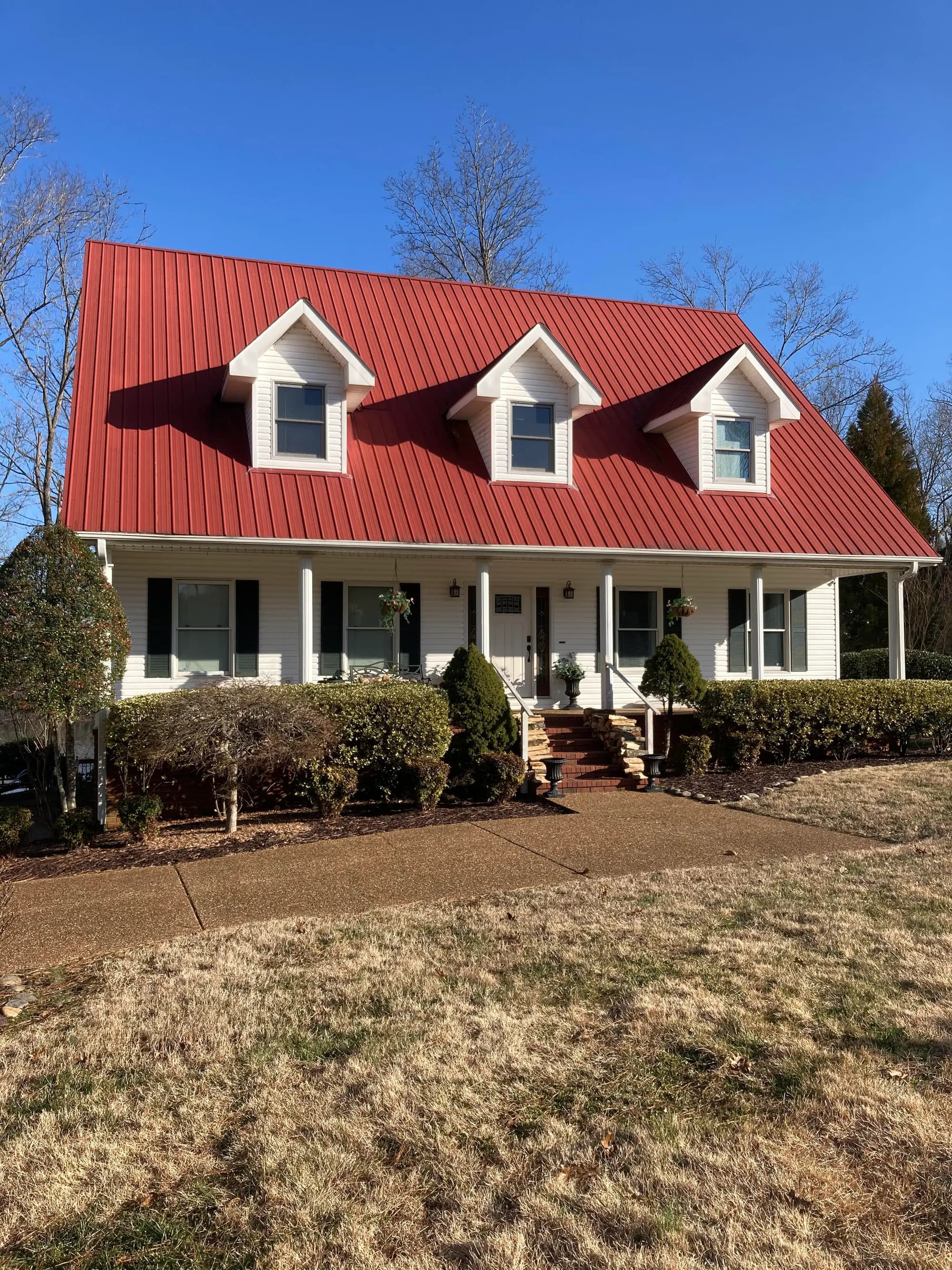 Cape-style home with a red metal roof, three dormers and a covered front porch