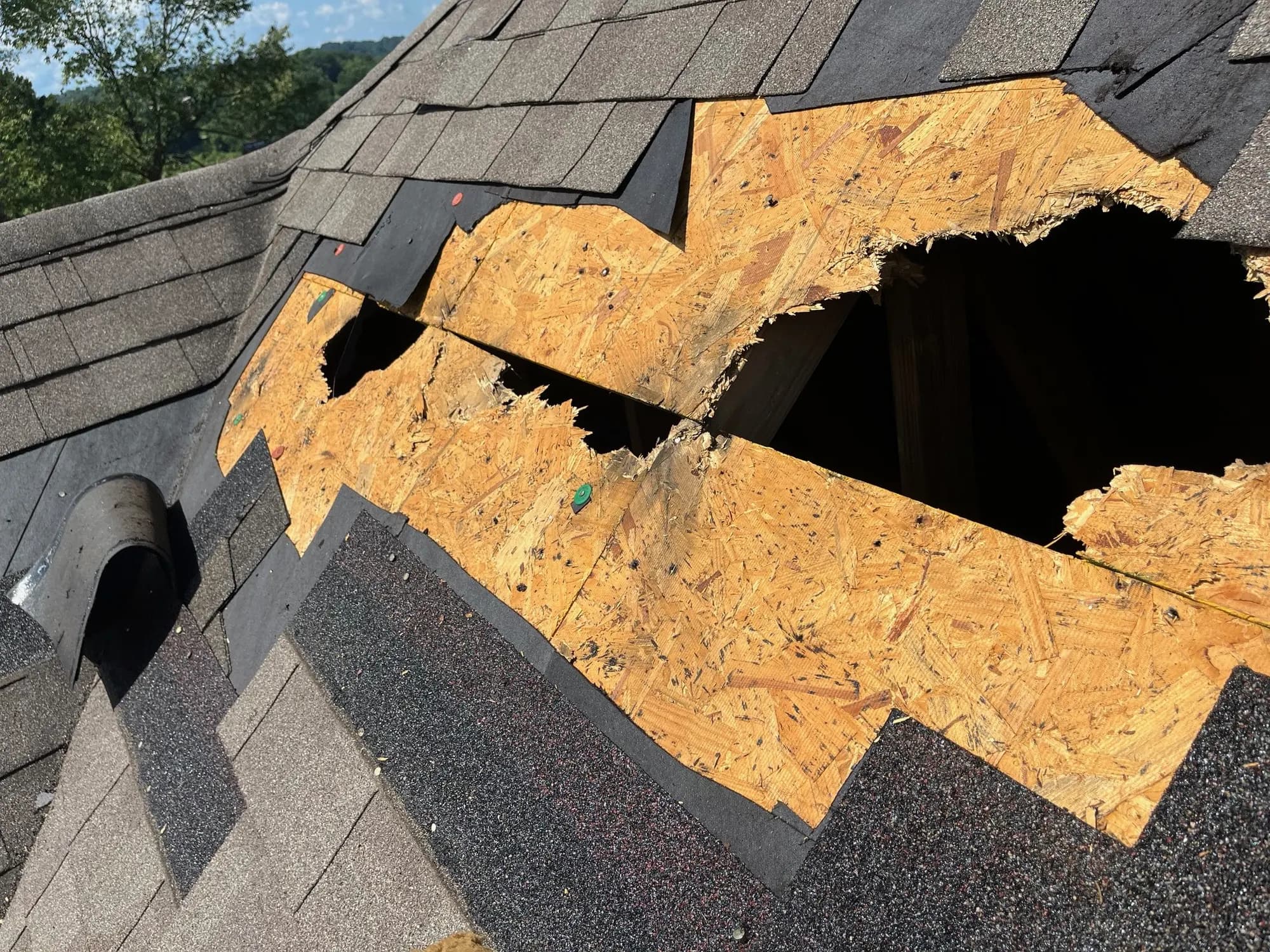 Storm-damaged shingle roof with a hole through the decking, before the emergency repair