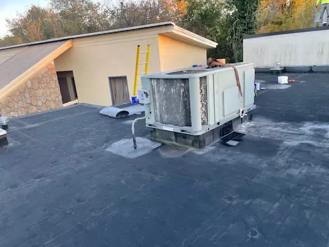 Black EPDM roof on a commercial building with a rooftop HVAC unit and a ladder set against the wall