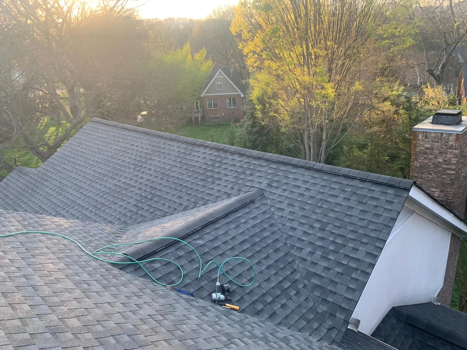 Aerial view of a newly shingled residential roof with a pneumatic nail gun and hose on the roof surface at sunset
