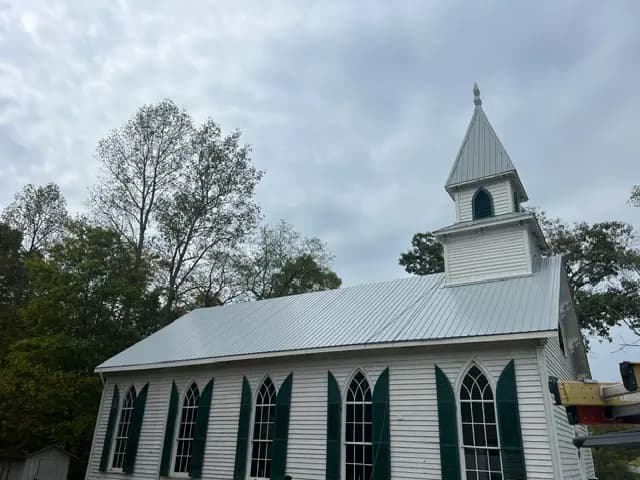 White country church with a steeple and green shutters under a newly installed silver metal roof