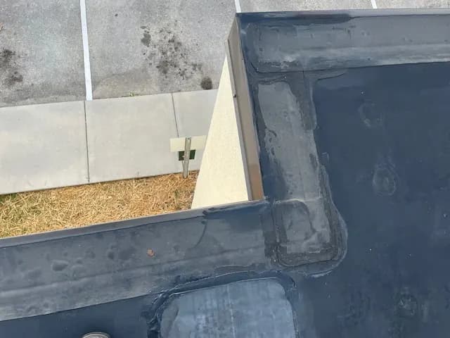 EPDM membrane flashing wrapped around a parapet corner on a commercial roof, with the parking lot below
