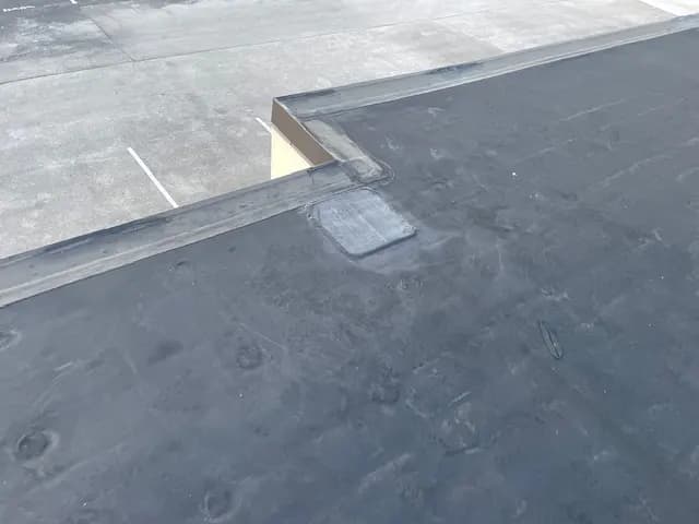 Black EPDM rubber membrane on a low-slope commercial roof with a repaired patch, the kind of roof a coating can extend