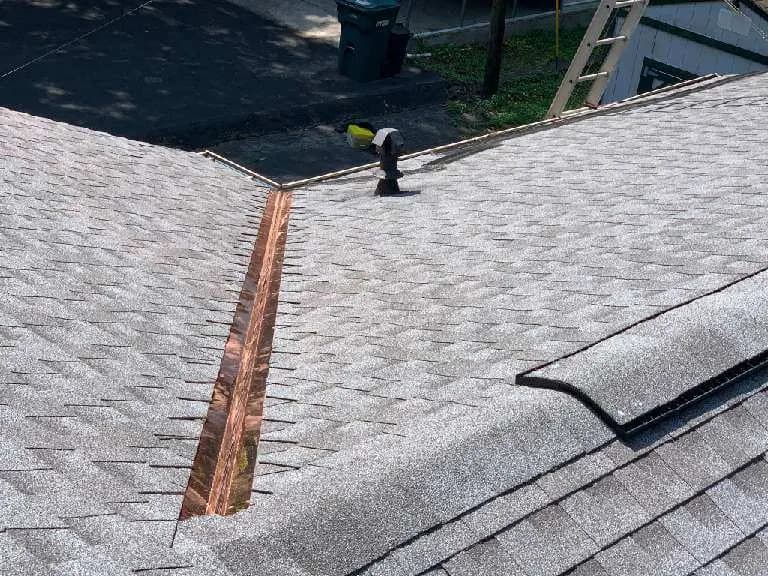 Roofer working on a valley flashing detail of a newly installed shingle roof, viewed from above