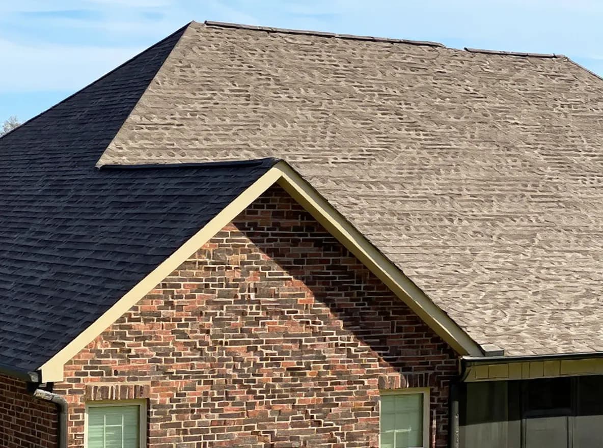 A brick house with a large, newly shingled dark gray roof and a screened-in porch area, set against a partly cloudy sky
