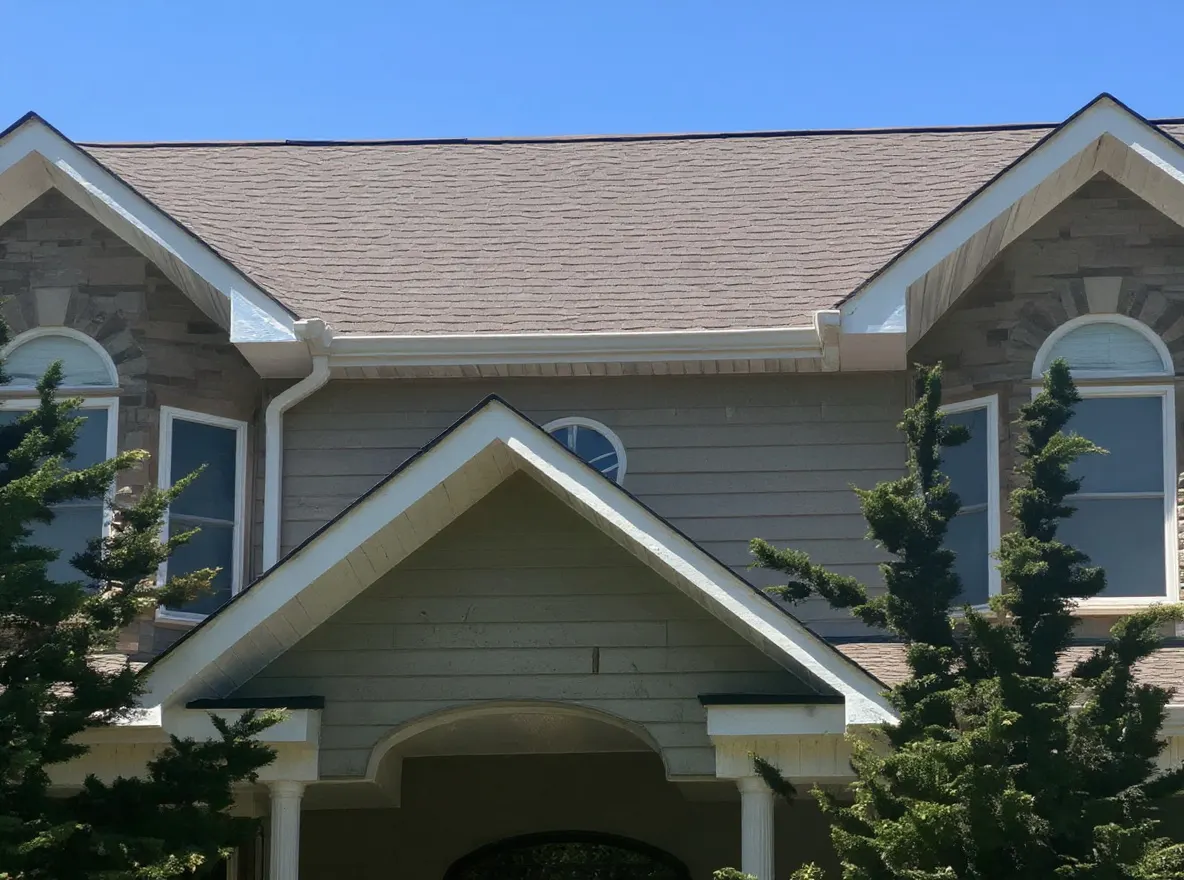 A large two-story house with stone and shingle siding, a wraparound porch, and a well-manicured lawn under a clear blue sky