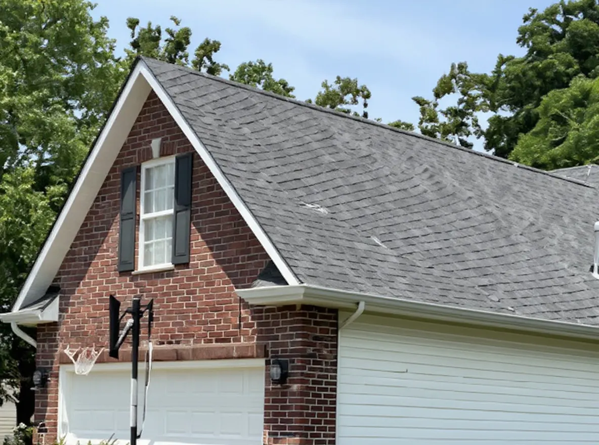 Closer view of the roof: a house exterior showing a red brick and white siding home with a gray shingle roof, landscaped garden beds, and a green lawn