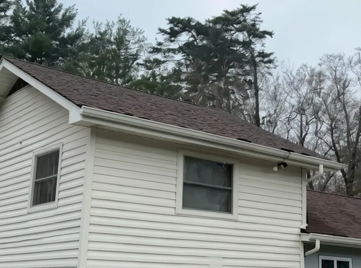 A single-story residential home with light-colored siding, an attached garage, brick chimney, and a driveway