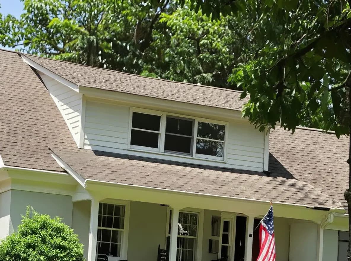 Closer view of the roof: a single-story home with a shingled roof and American flag, surrounded by a lush lawn and mature trees