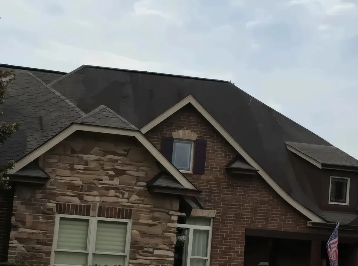 A large brick and stone two-story home with a dark shingled roof, featuring a curved driveway, landscaping, and two vehicles parked in front