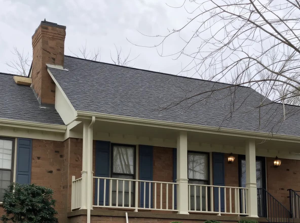 A single-story brick ranch home with a newly installed dark gray shingle roof, viewed from the driveway with a ladder and roofing debris visible on the lawn