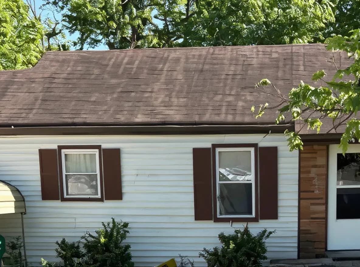 Exterior view of a single-story ranch house with a shingled roof, brick and siding facade, and a large front lawn shaded by trees