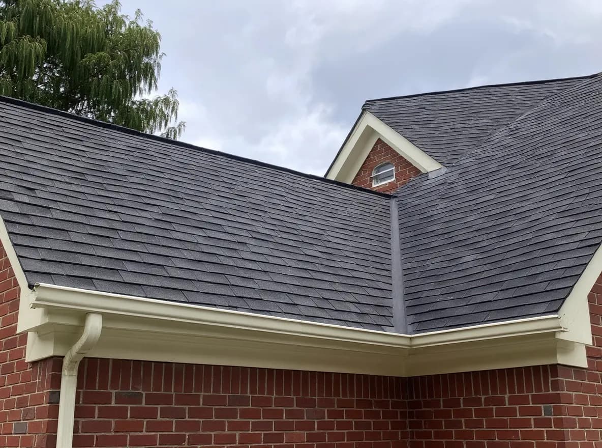 Exterior view of a brick two-story home with a gray asphalt shingle roof, gutters, and attached garage under a cloudy sky